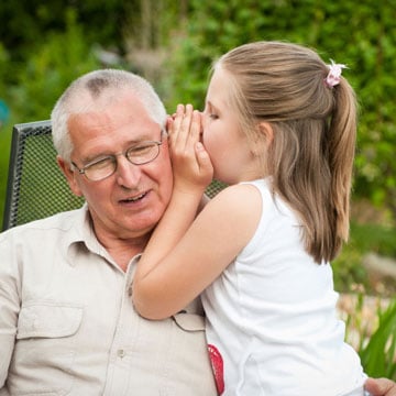 A little girl whispering in her grandpa's ear