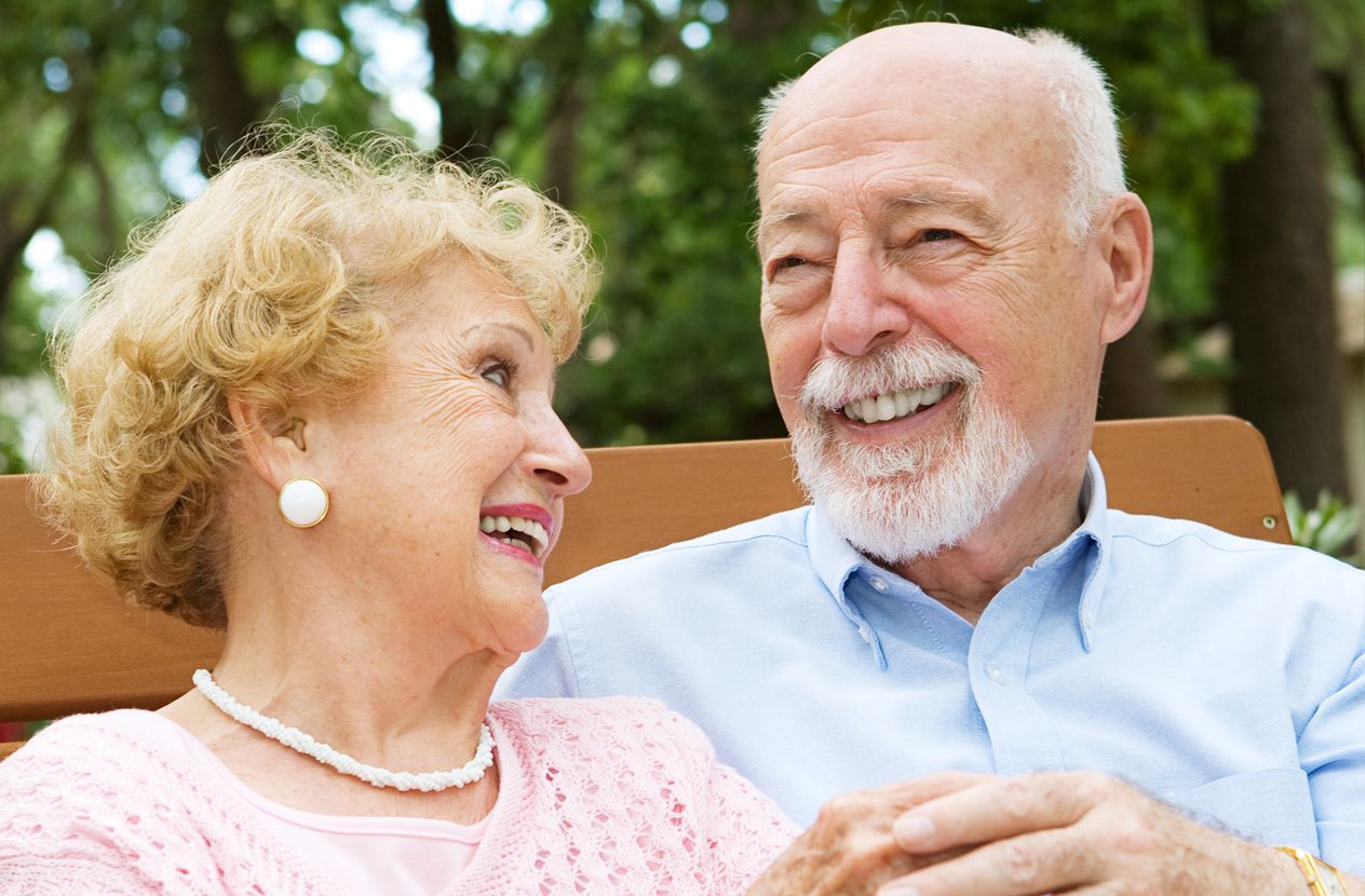 An elderly couple laughing on a park bench