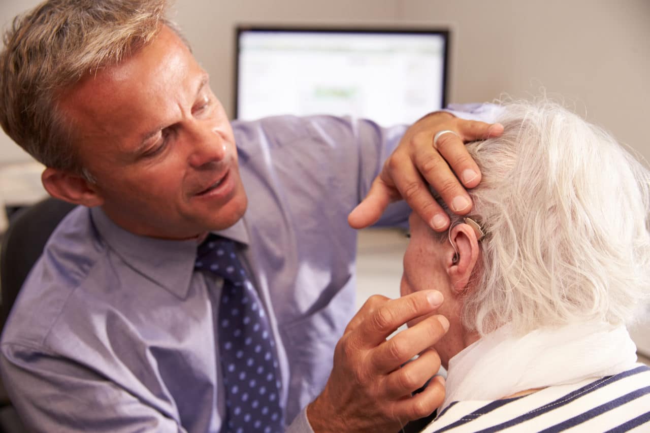 audiologist fitting a man with a hearing aid
