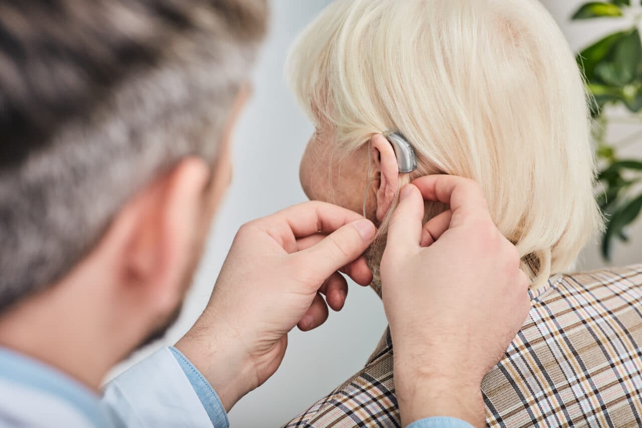 Audiologist fitting an older woman with a hearing aid.