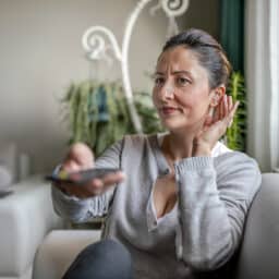 Woman with a hand to her ear watching tv