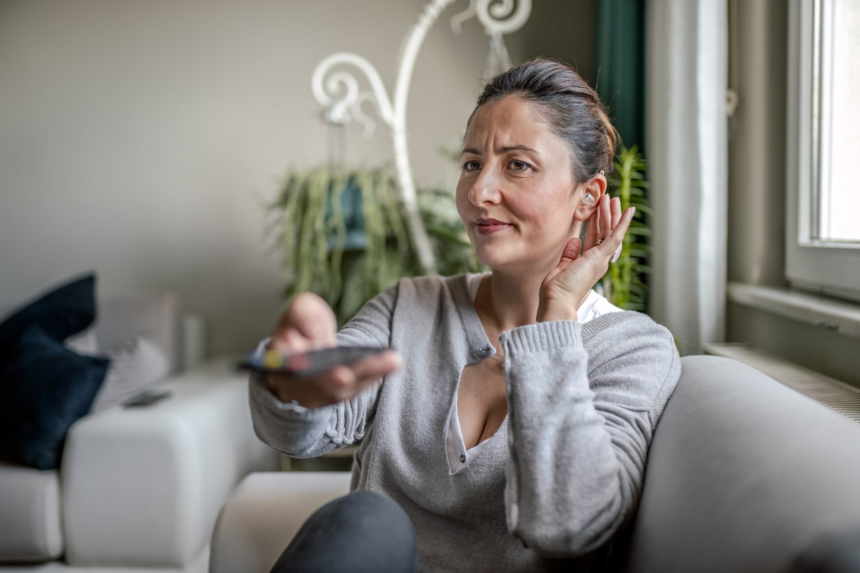 Woman with a hand to her ear watching tv.